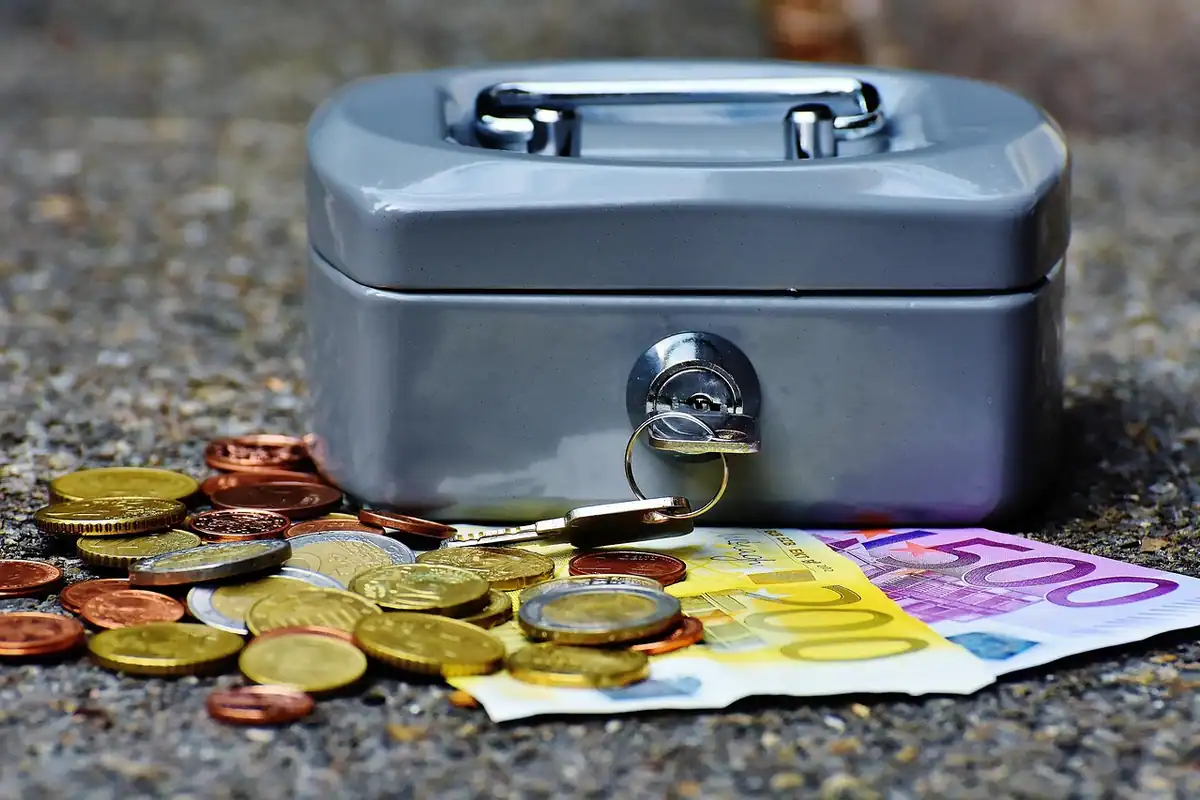 Bancnote și monede euro puse laolaltă, alături de o casetă pentru bani