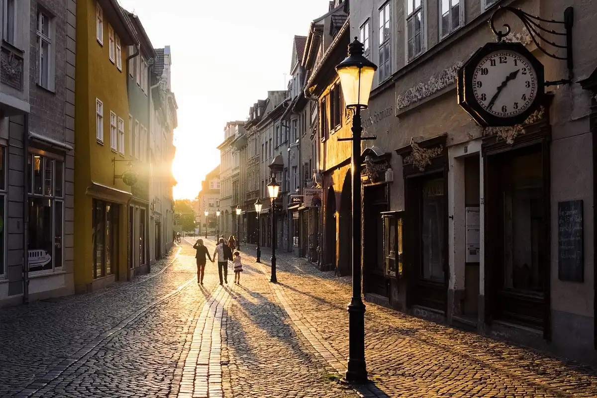 Stradă veche de oraș luminată de soarele la apus, cu oameni la plimbare