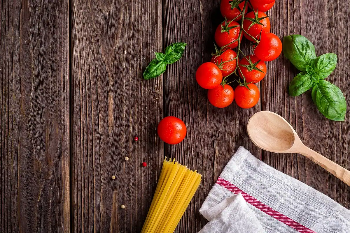 Masă rustică din lemn cu paste, roșii, busuioc și o lingură de lemn