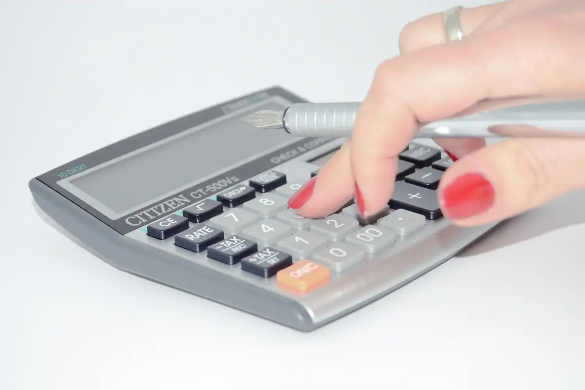 Mână care folosește un calculator de buzunar pe un birou, cu un pix alături