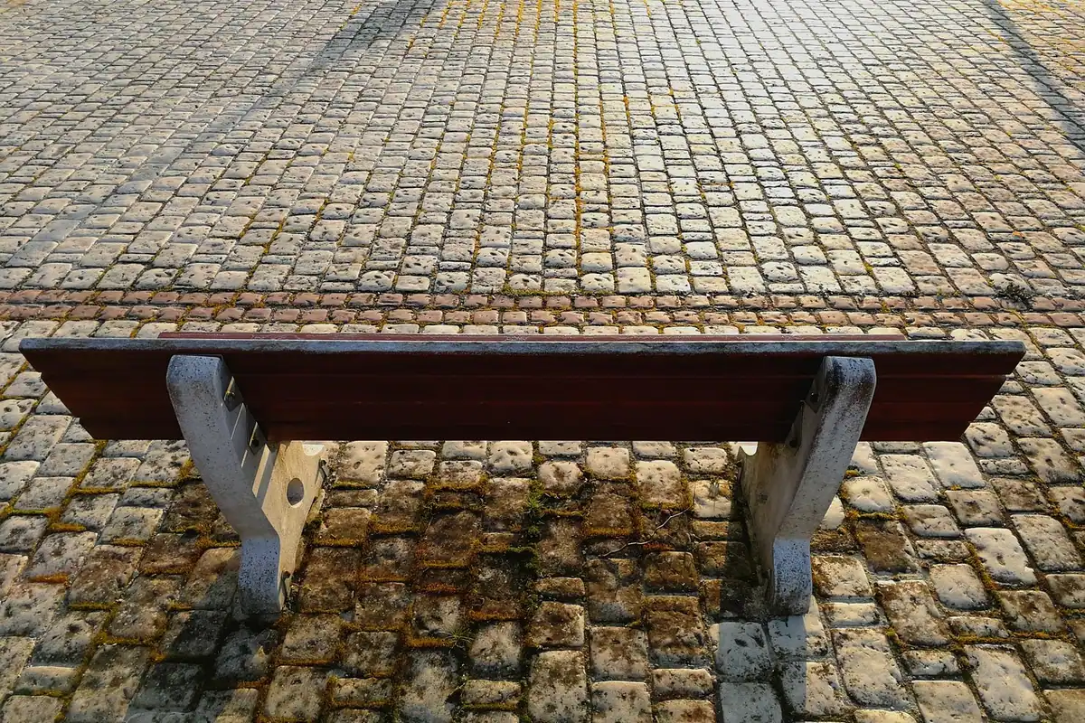 Bancă publică într-un spațiu pavat, văzută în perspectivă, loc de relaxare