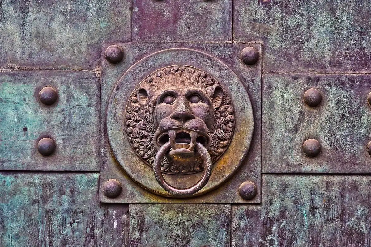 Ciocan de ușă din metal în formă de cap de leu, montat pe o ușă veche