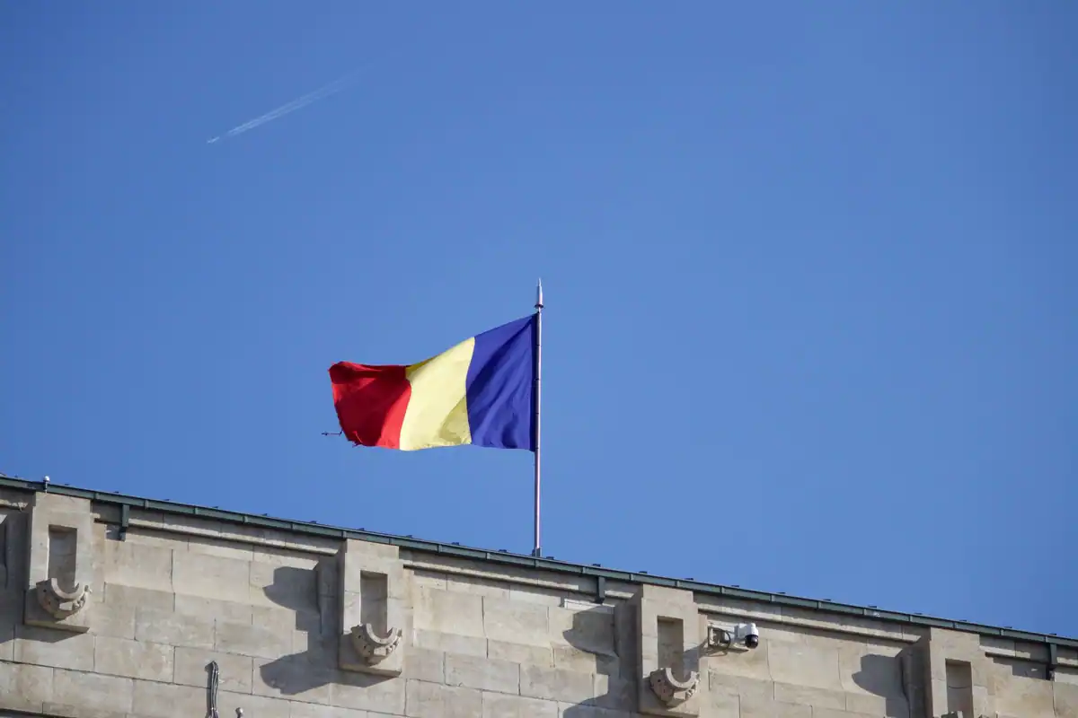 Drapelul României fluturând pe cer albastru deasupra unei clădiri