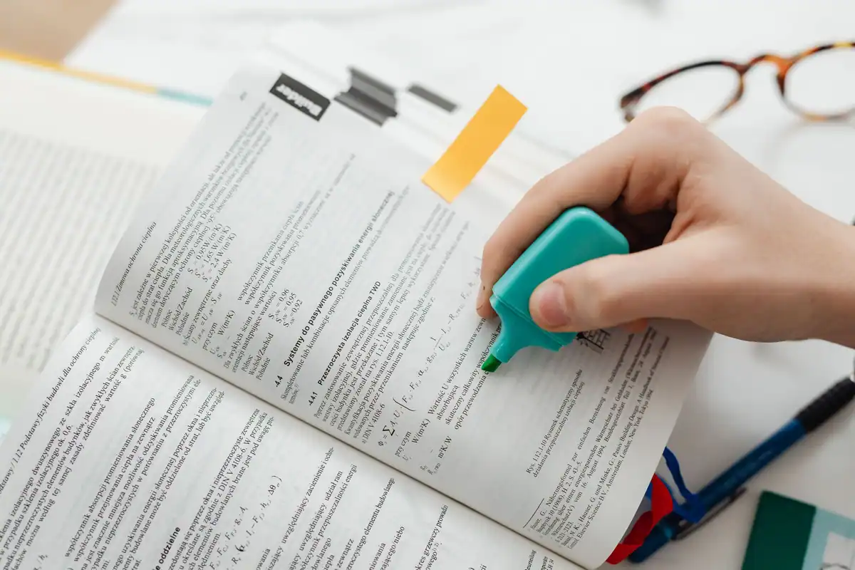 Mână care subliniază cu marker un text dintr-un manual deschis