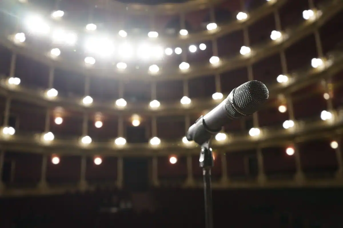 Microfon pe o scenă, cu luminile unei săli de spectacol în fundal
