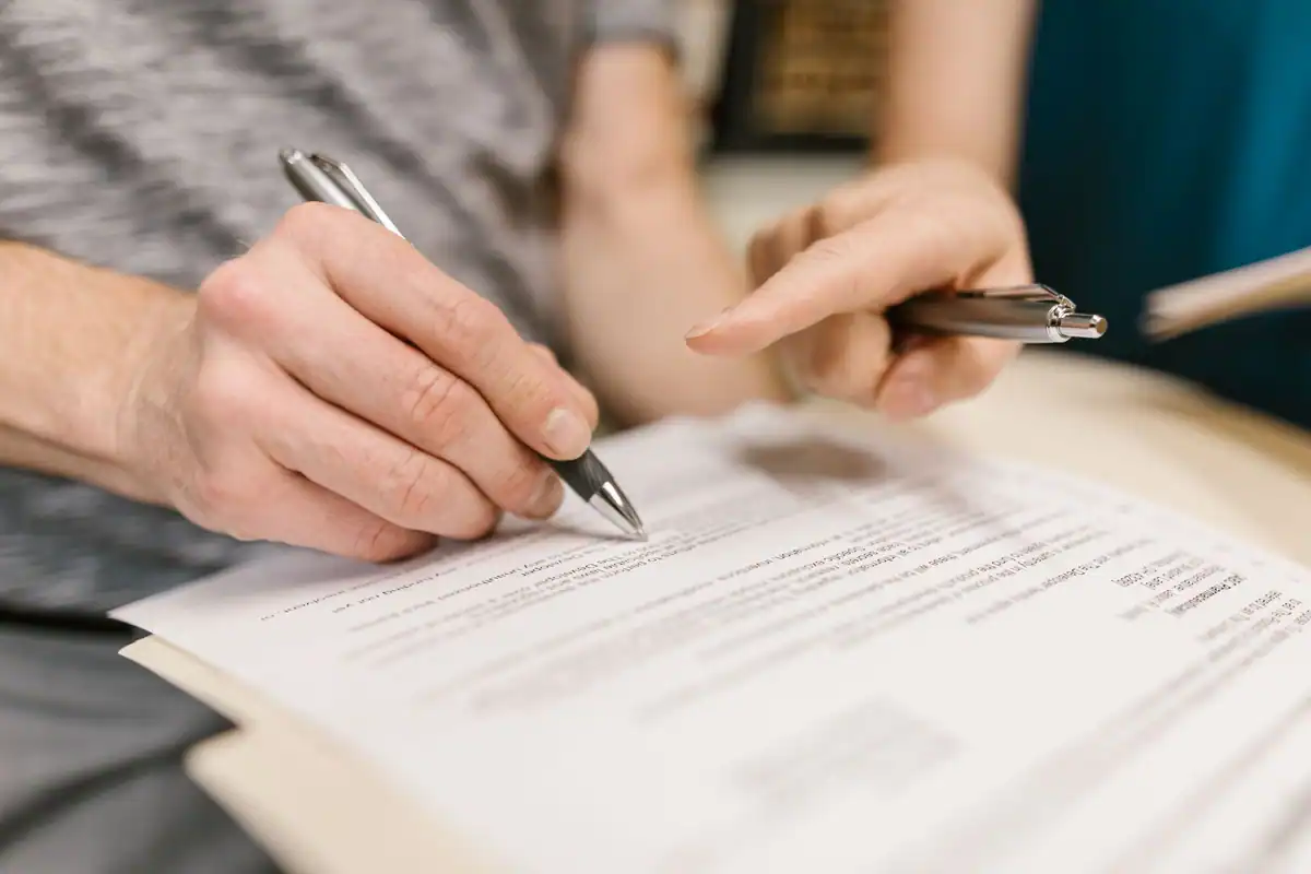 Două persoane citesc și semnează un document oficial, cu pixuri în mână