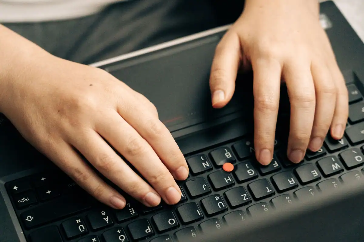Mâini pe tastatura unui laptop negru în timpul scrierii unei petiții