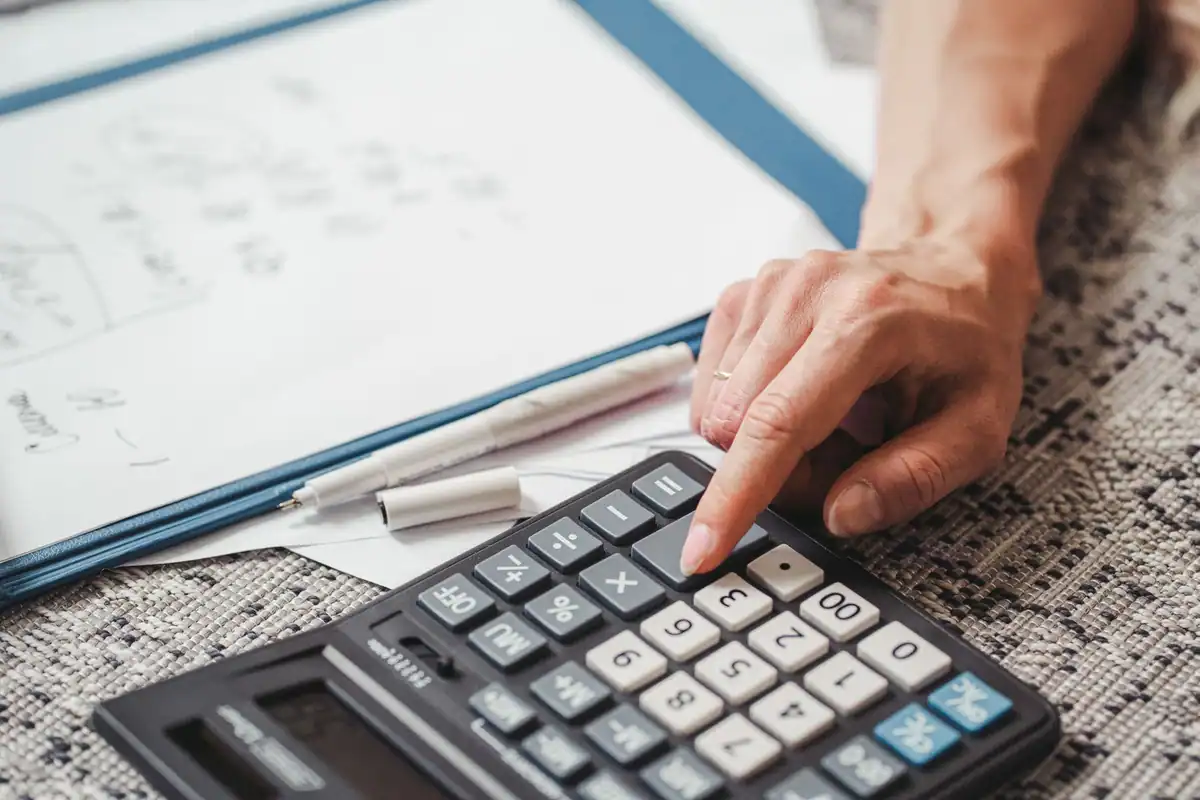 Mână care calculează pe un calculator, deasupra unor documente