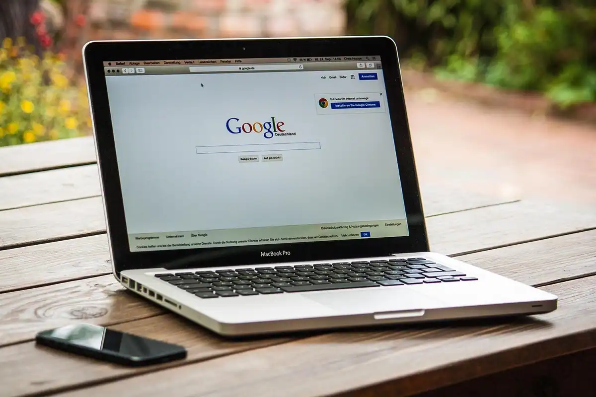 Laptop pe un birou, cu un browser deschis pe ecran, lângă un telefon